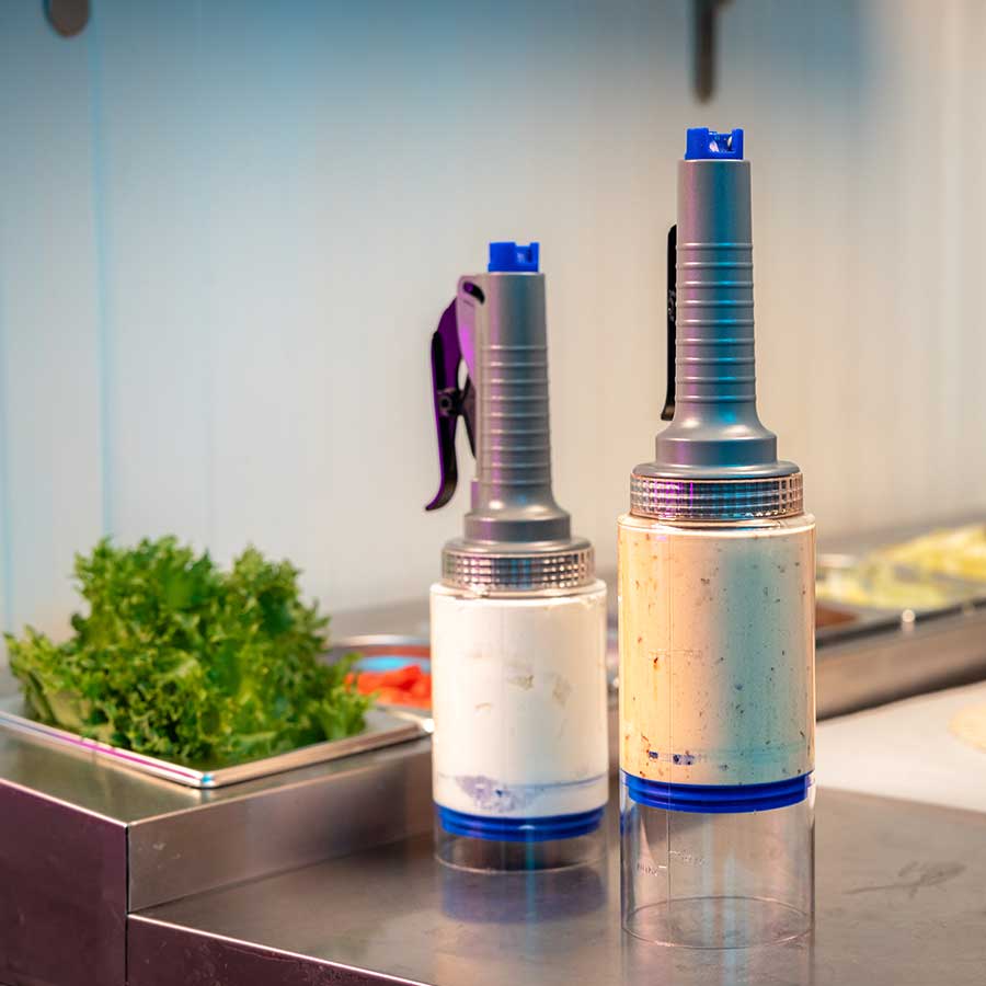 Showing two Portion Pump MAX dispensers inverted on a kitchen prep-table.